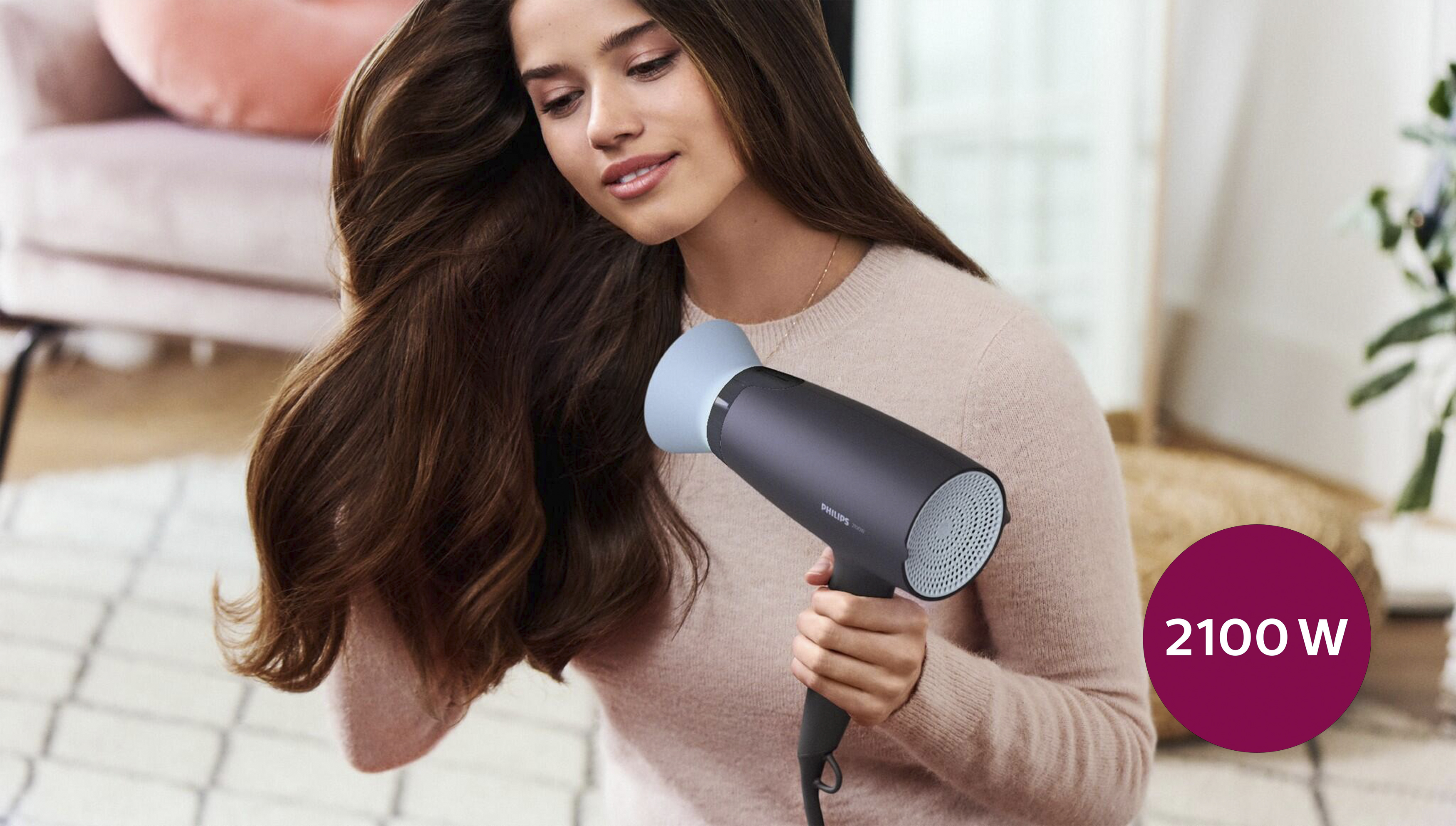 Una mujer peinándose con un secador de pelo negro y azul. Es de 2100W.