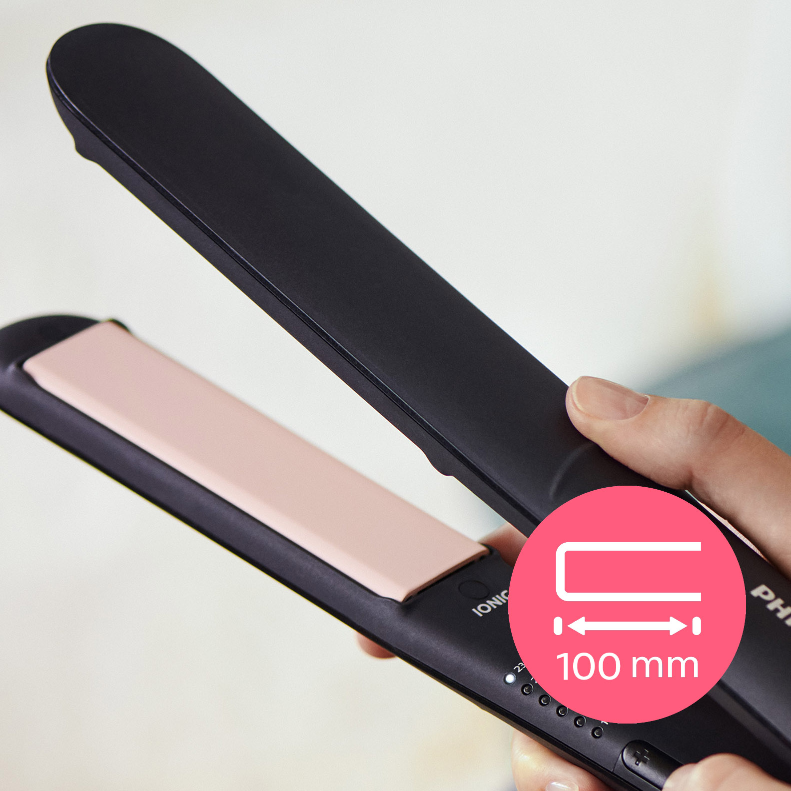 Una persona sosteniendo una plancha de pelo negra con una placa calefactora rosa.