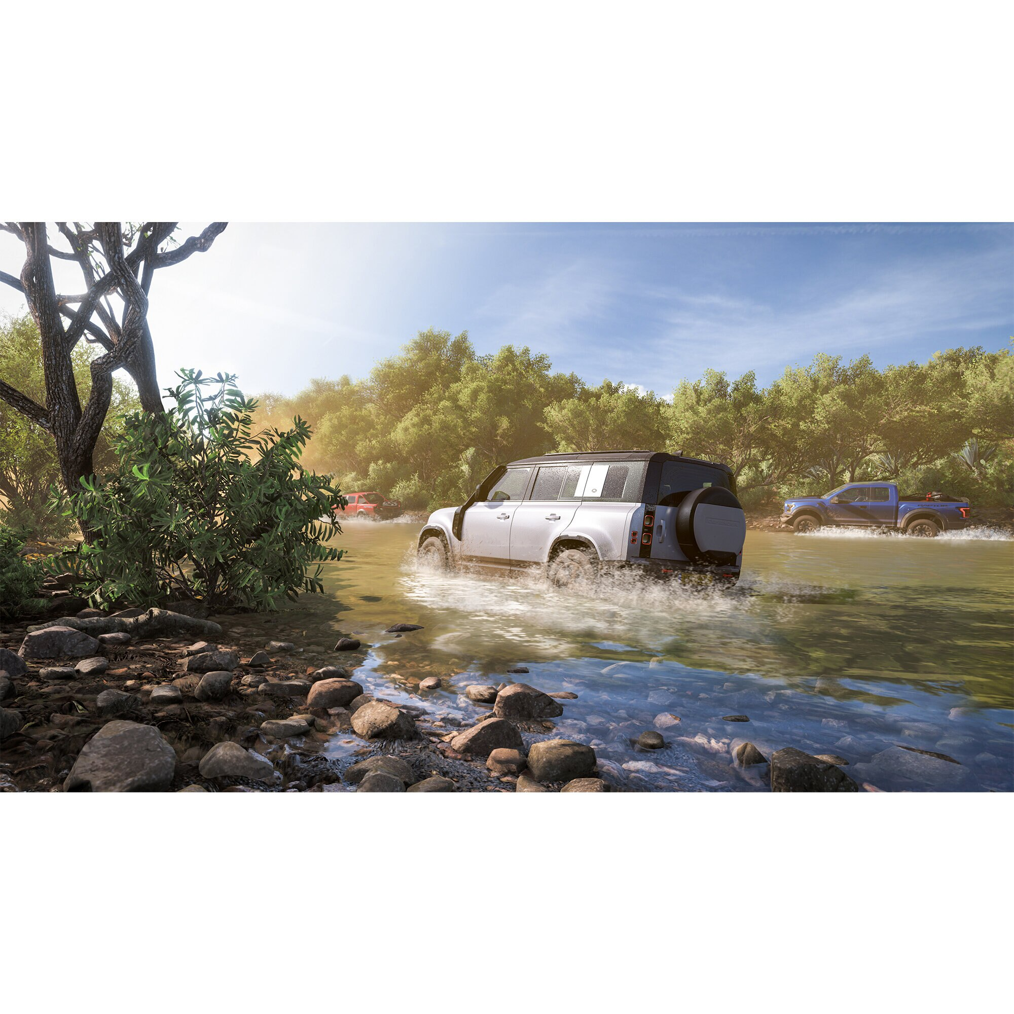Biały Land Rover jedzie przez rzekę, z niebieską ciężarówką w tle. Drzewa wzdłuż brzegów.