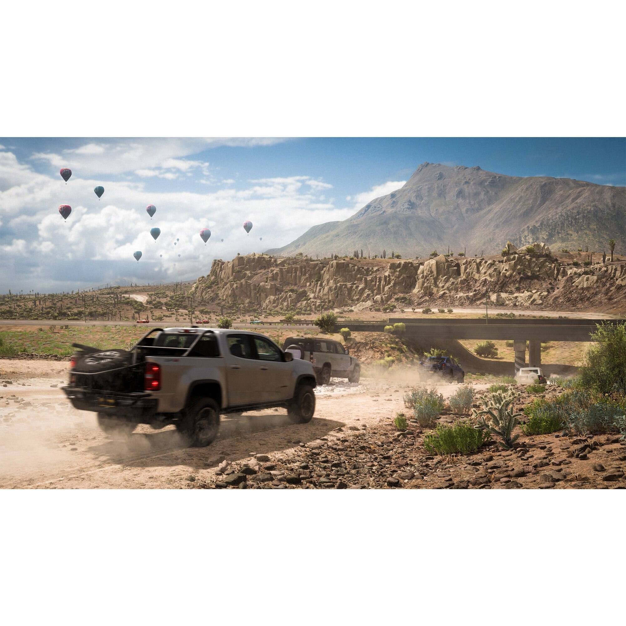 Samochody terenowe ścigają się na polnej drodze, z balonami na gorące powietrze w tle, pod błękitnym niebem.