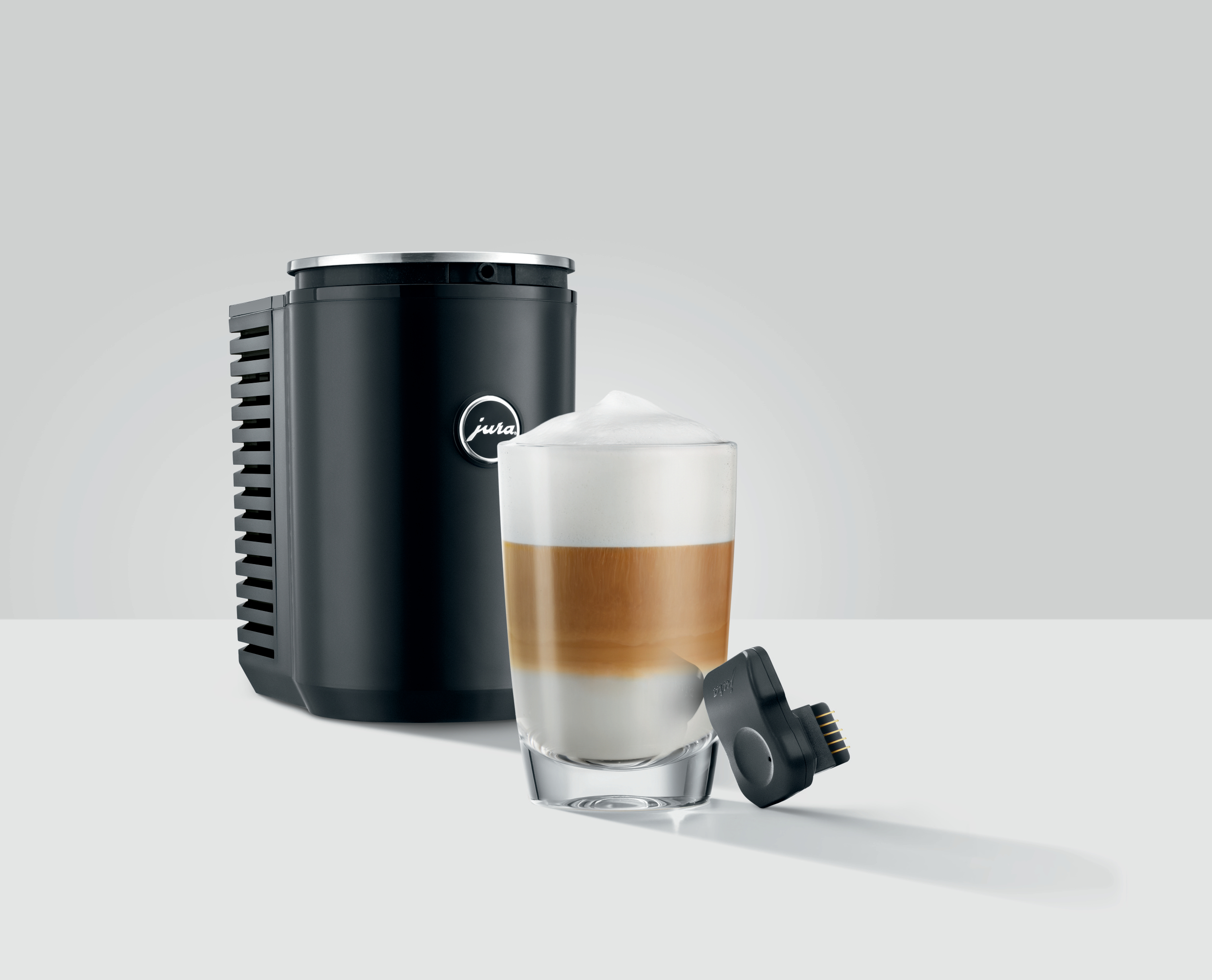 Eine schwarze Jura Kaffeemaschine mit einem Glas geschichteten Kaffees und Zubehör.