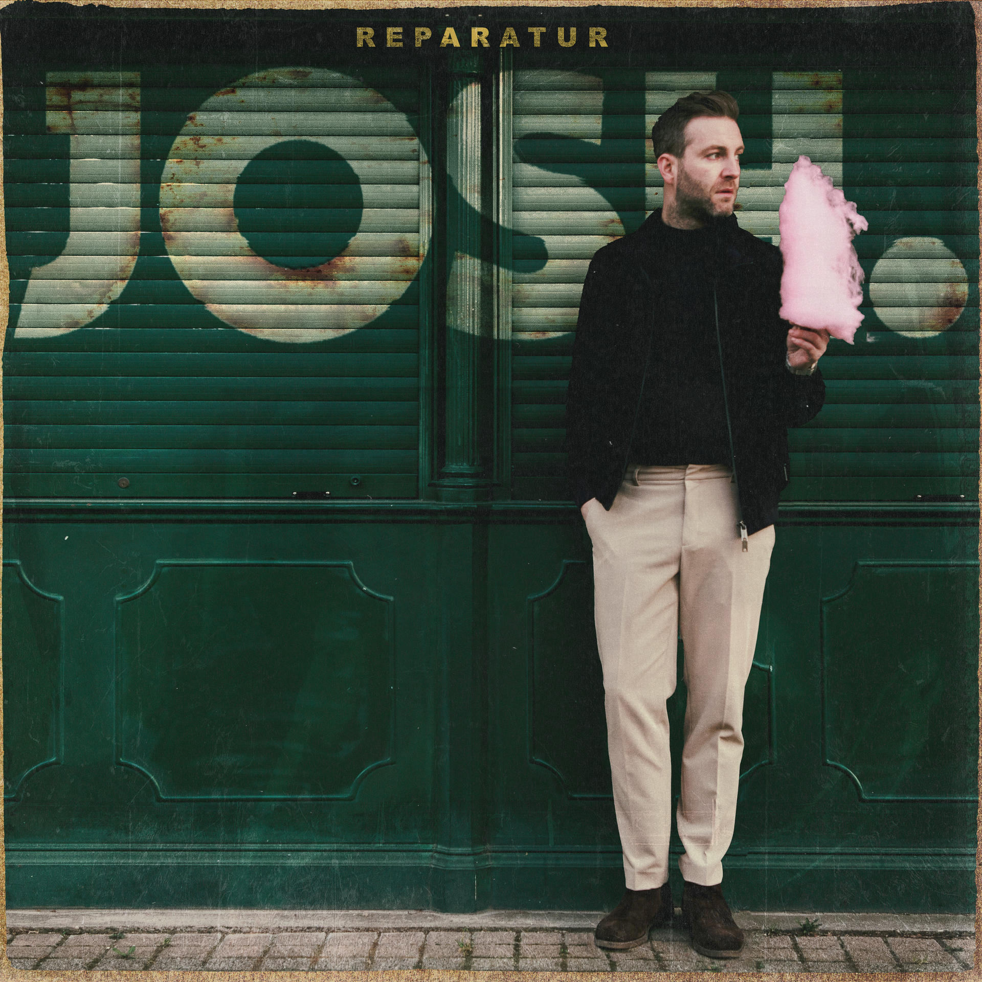 Mann hält rosa Zuckerwatte vor grünen Fensterläden mit dem Wort 'JOSH'.