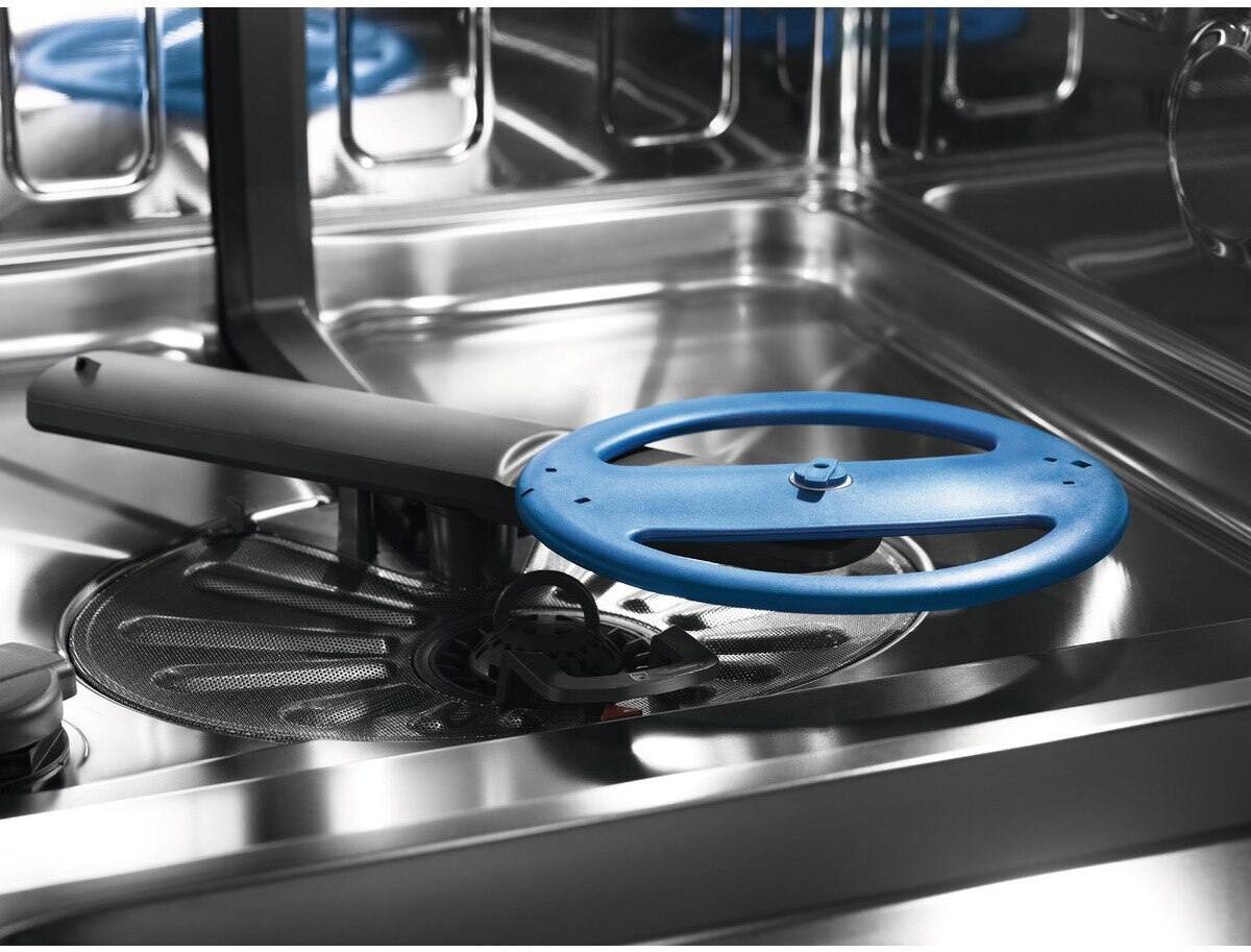 Wnętrze zmywarki z niebieskim obrotowym ramieniem natryskowym i filtrem.