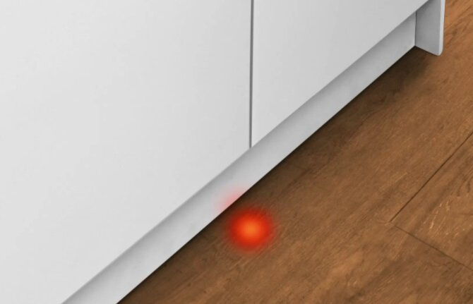 Czerwone światło na podłodze pod białą szafką. Drewniana podłoga.