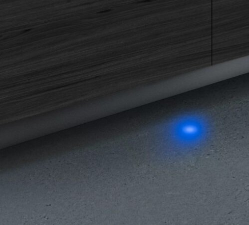 Ciemna drewniana powierzchnia zwisa nad szarą ścianą. Małe, jasnoniebieskie światło świeci na ścianie.