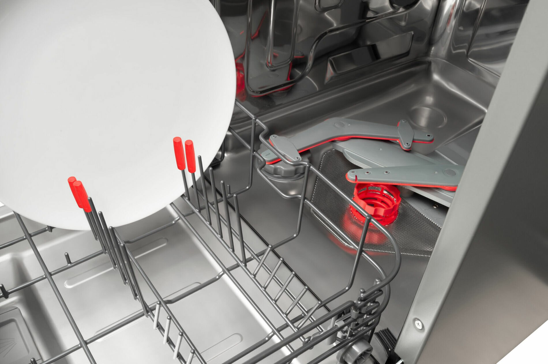 Wnętrze zmywarki z białym talerzem spoczywającym na stojaku. Widoczne czerwone plastikowe części.