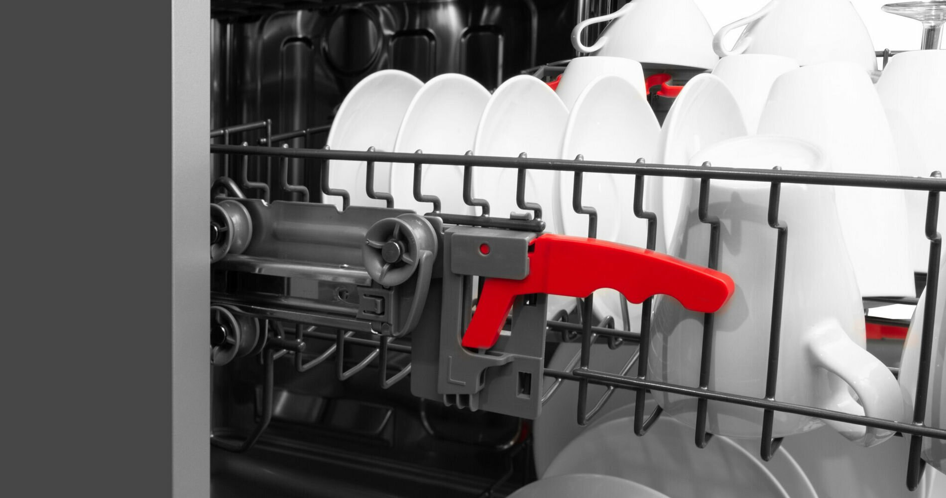 Wnętrze zmywarki z naczyniami i filiżankami. Widoczny jest czerwony uchwyt.
