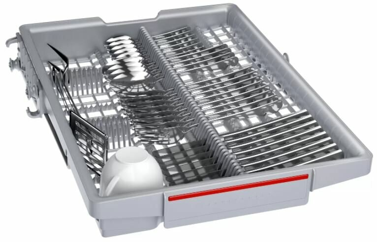 Koszyk zmywarki z naczyniami, sztućcami i białym kubkiem w środku.