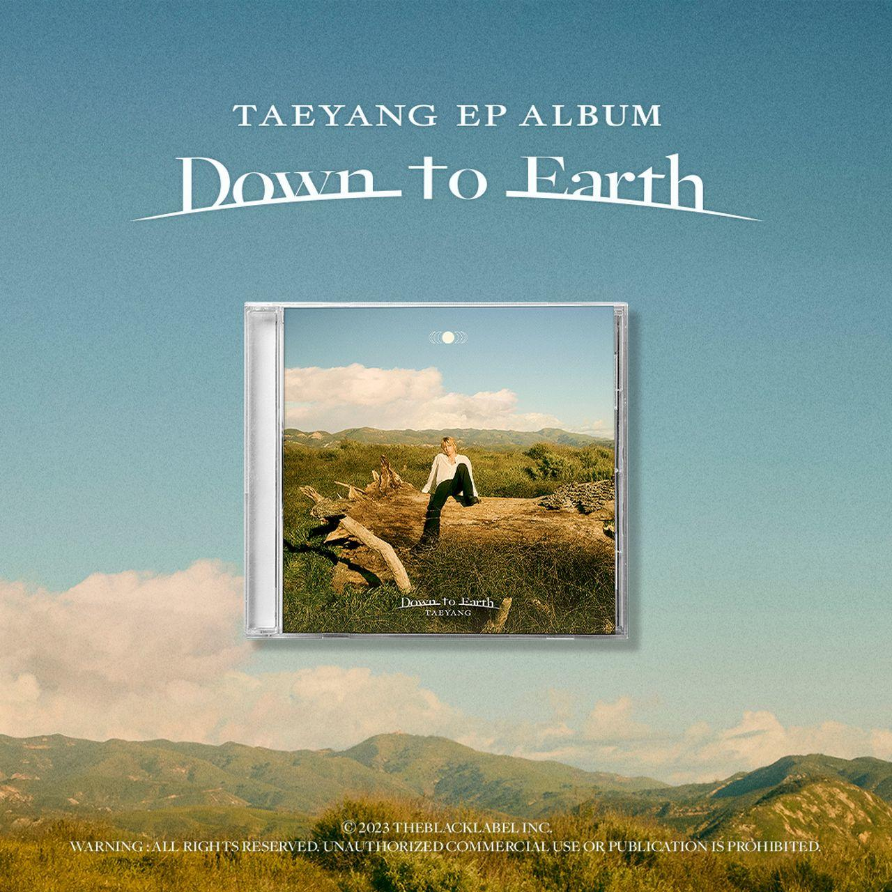 Albumcover 'Down to Earth' von Taeyang, CD-Hülle auf einem Baumstamm, Berge im Hintergrund, blauer Himmel.