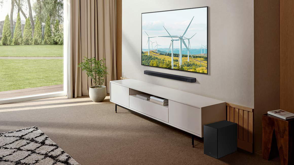 Ein Fernseher auf einem weißen Ständer mit einer Soundbar und einem Subwoofer in einem Wohnzimmer.