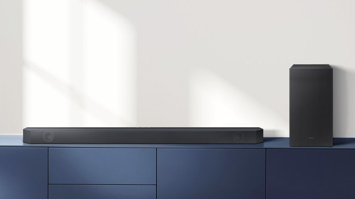 Eine schwarze Soundbar und ein Subwoofer auf einem blauen Schrank vor einer weißen Wand. Modernes und minimalistisches Design.