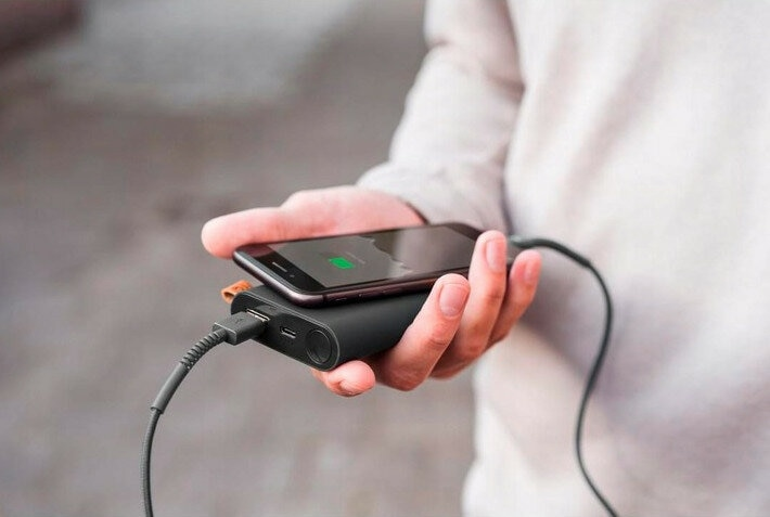 Dłoń trzymająca czarny power bank, ładujący czarny telefon kablem.