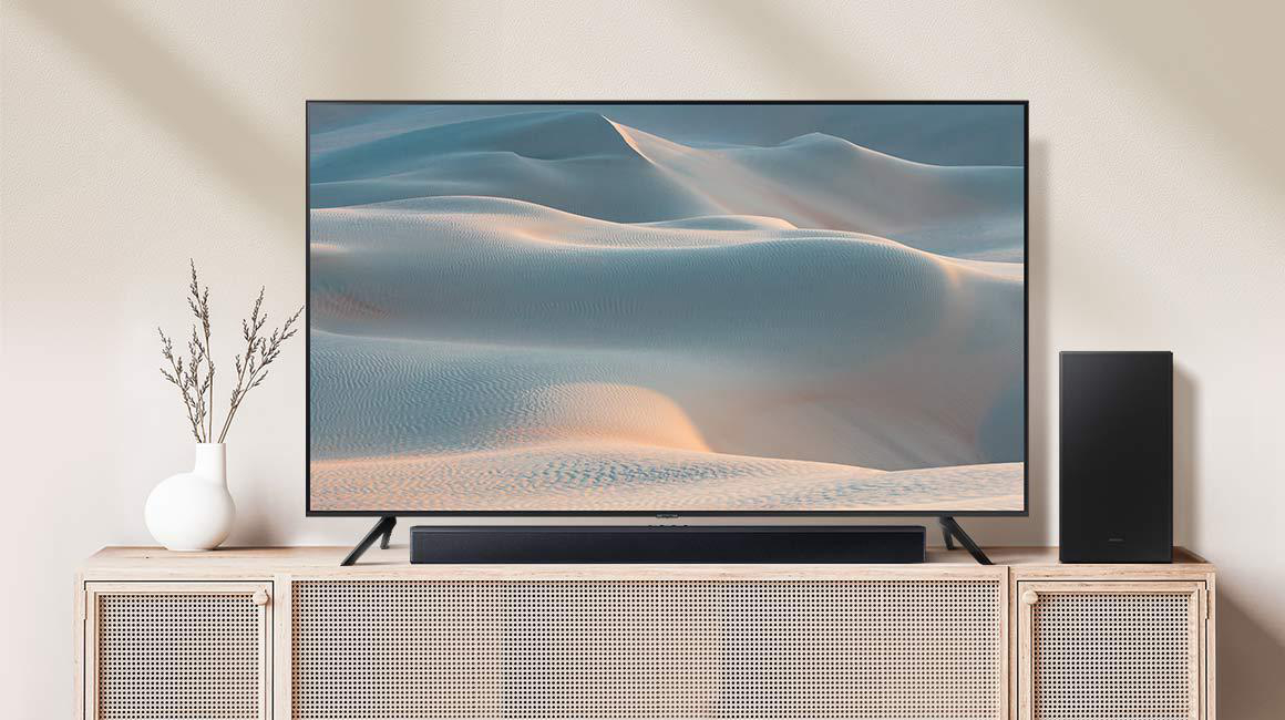 TV auf einem Holzschrank mit Soundbar und Lautsprecher. Hintergrund ist Wüstenlandschaft.