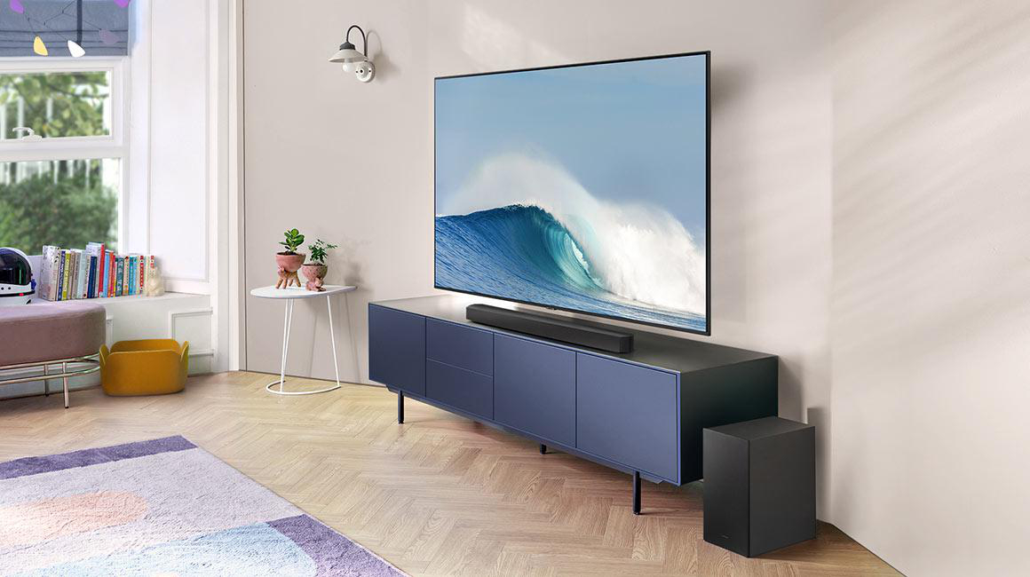 Wohnzimmer mit Fernseher auf blauem Schrank, Soundbar, Subwoofer und Teppich.