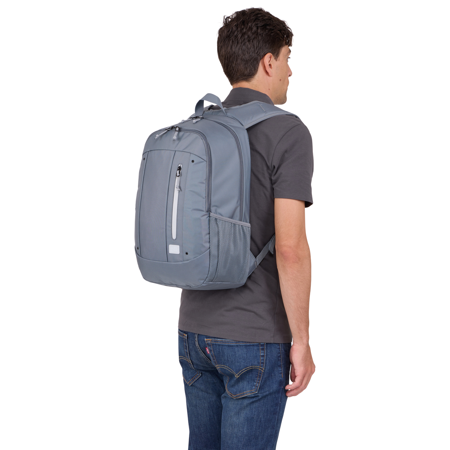 A man wearing a grey backpack and a grey shirt, with blue jeans, from behind.