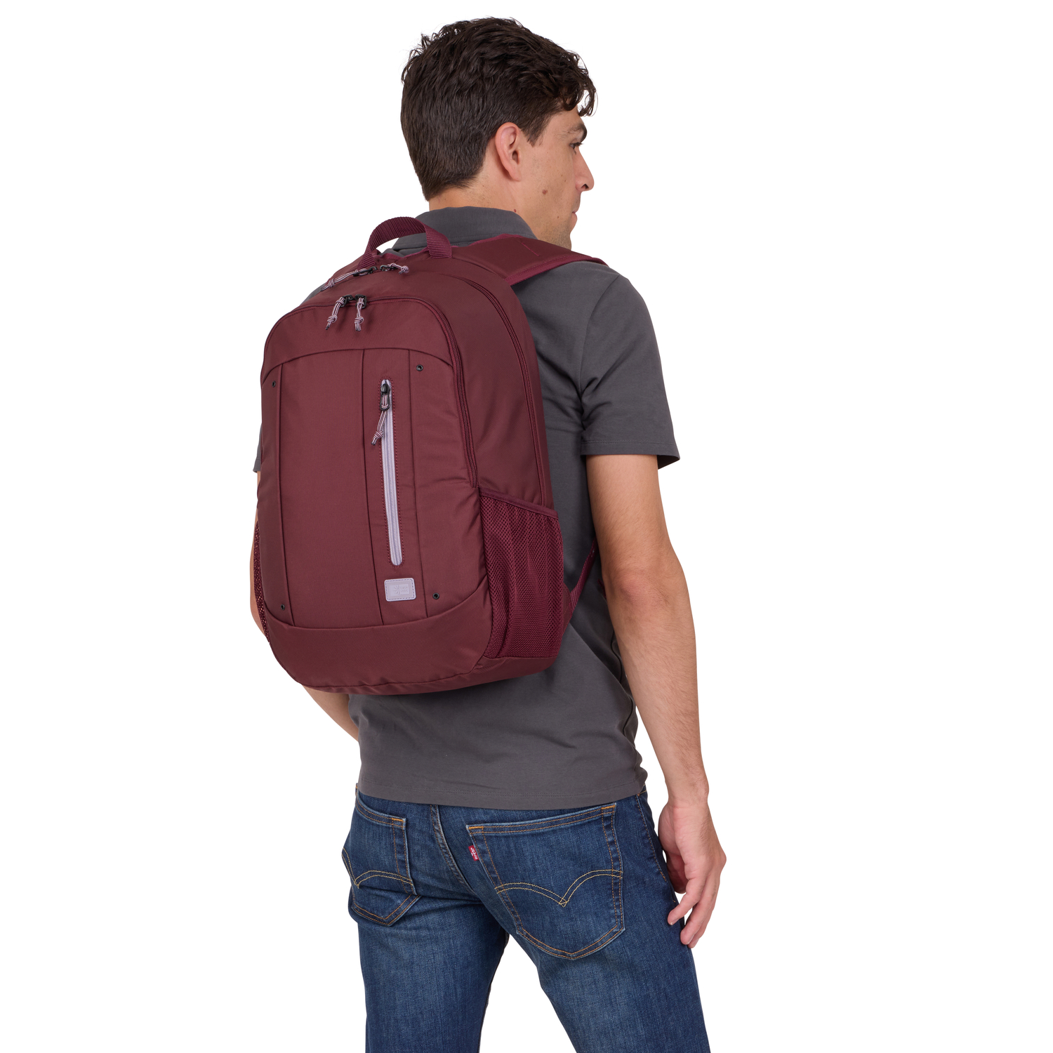 A man with a maroon backpack, wearing a gray shirt and blue jeans, seen from the back.