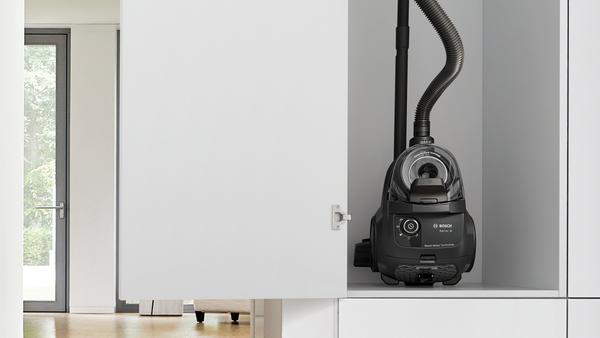 Ein schwarzer Staubsauger wird in einem weißen Schrank aufbewahrt, die Tür ist teilweise geöffnet.