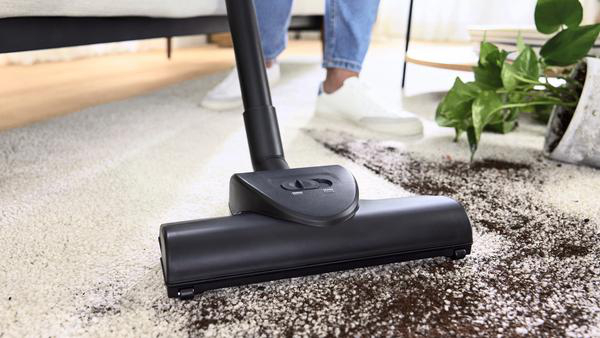Person saugt Teppich mit dunkel gefärbtem Staubsaugerkopf.