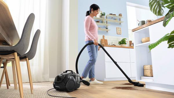 Frau, die einen Holzboden saugt. Staubsauger, Schlauch und ein paar schmutzige Stellen sichtbar.