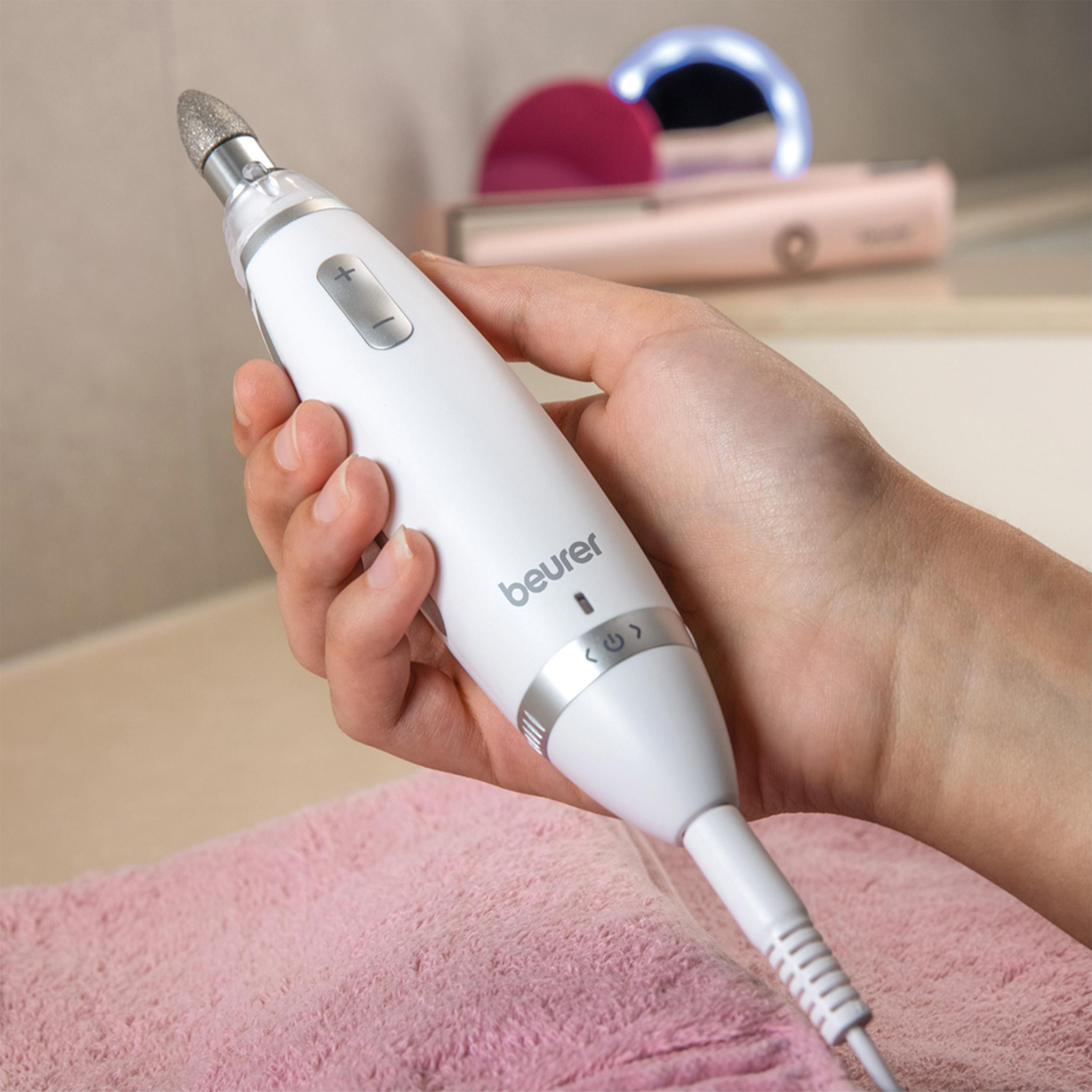 Eine Hand hält ein weißes Nagelpflegegerät. Es hat einen rotierenden Kopf und Steuertasten. Rosa Handtuch im Hintergrund.