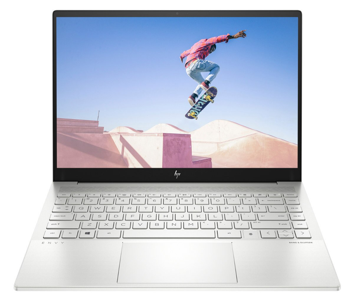 Srebrny laptop HP otwarty, ekran pokazuje deskorolkarza w powietrzu. Klawiatura widoczna, tło park.