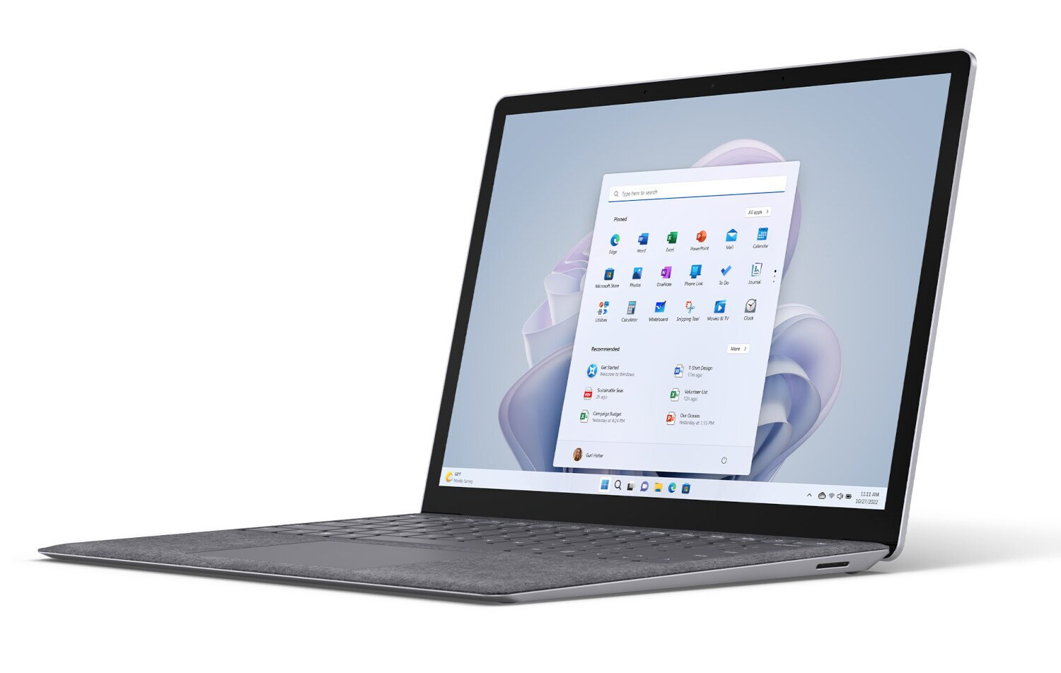 Szary laptop z otwartym ekranem wyświetlającym interfejs Windows 11. Laptop leży na białej powierzchni.