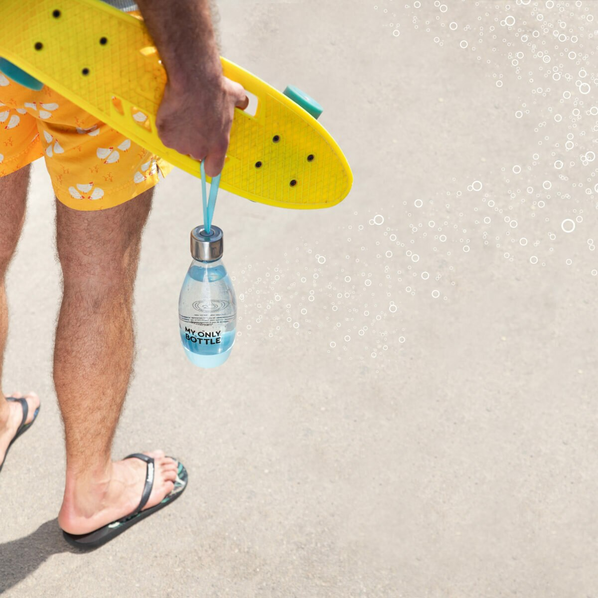 Osoba trzyma deskorolkę i butelkę wody. Osoba ma na sobie szorty i sandały.
