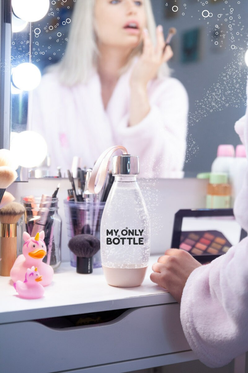 Kobieta nakłada makijaż przed lustrem, na stole butelka z wodą.