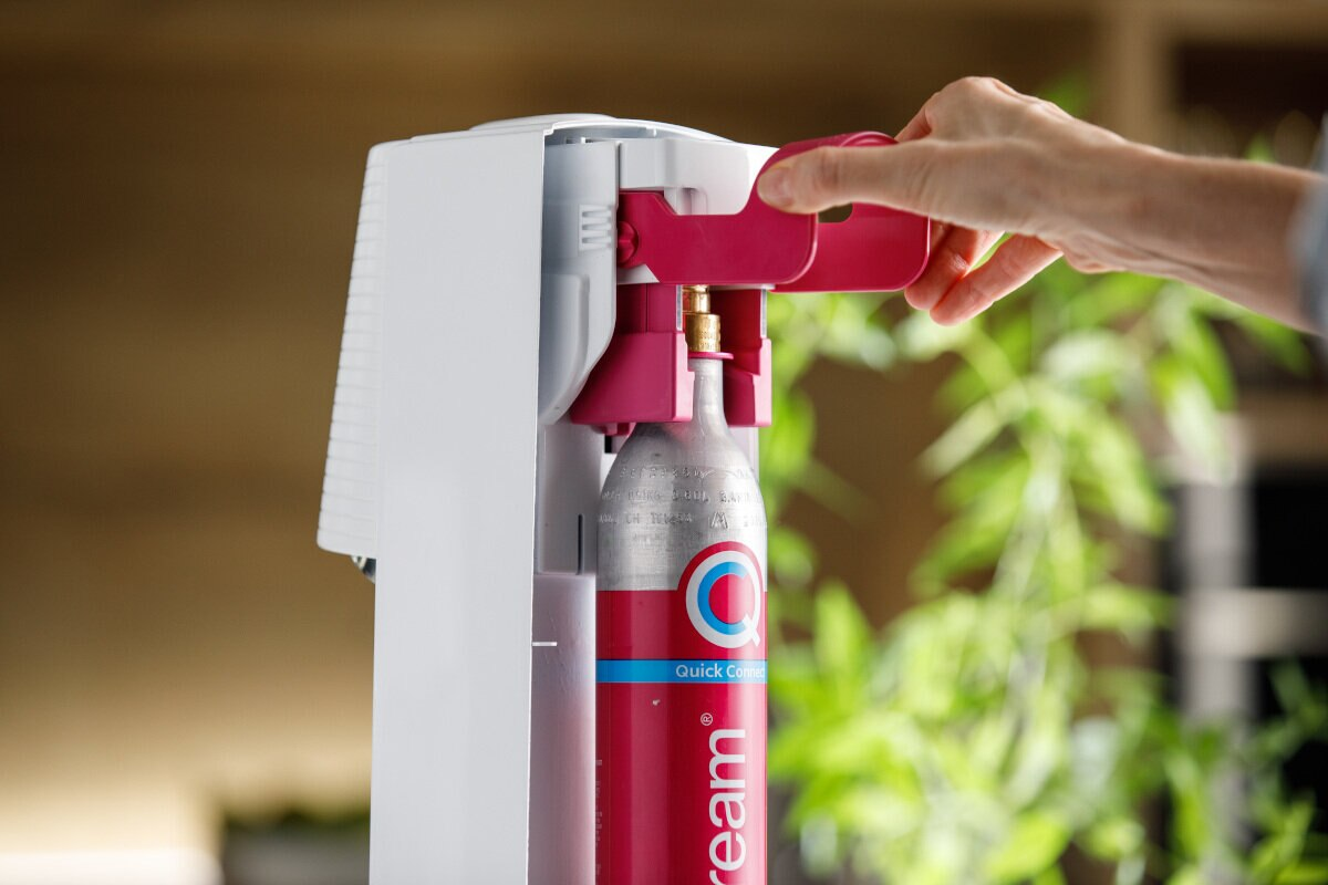 Osoba ładująca butelkę wody do białej i różowej maszyny do produkcji sody.