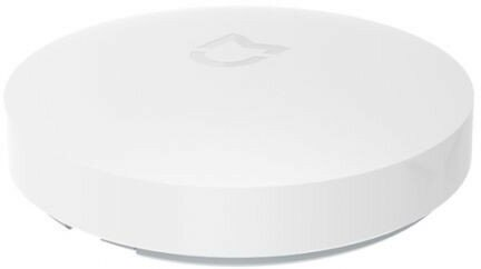 Białe, okrągłe urządzenie z lekko podniesioną górą. Widoczne subtelne logo. Urządzenie znajduje się na białej powierzchni, dobrze oświetlone.