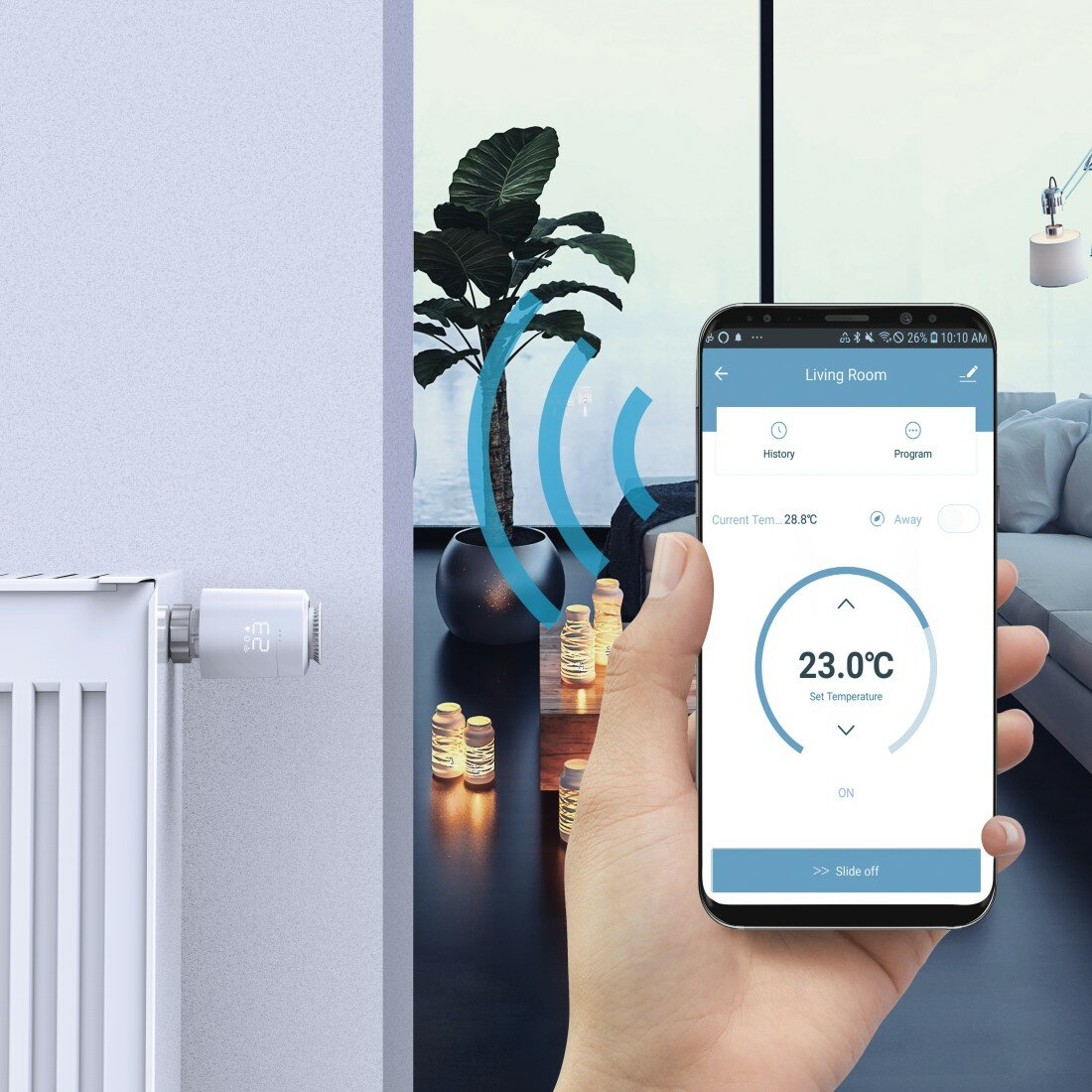 Dłoń trzymająca smartfon kontroluje temperaturę. Grzejnik i roślina w tle.