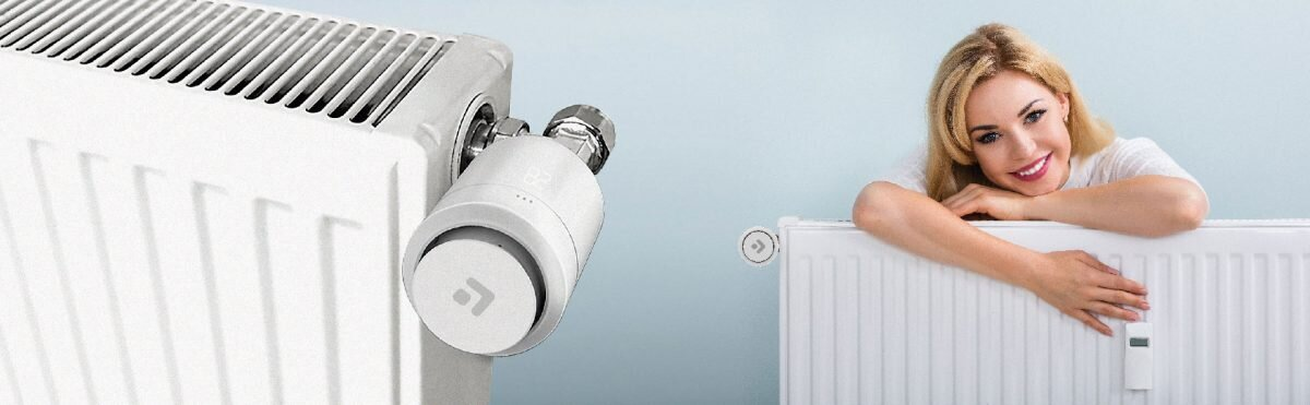 Kobieta uśmiecha się obok białego grzejnika z inteligentnym termostatem. Jasnoniebieskie tło.