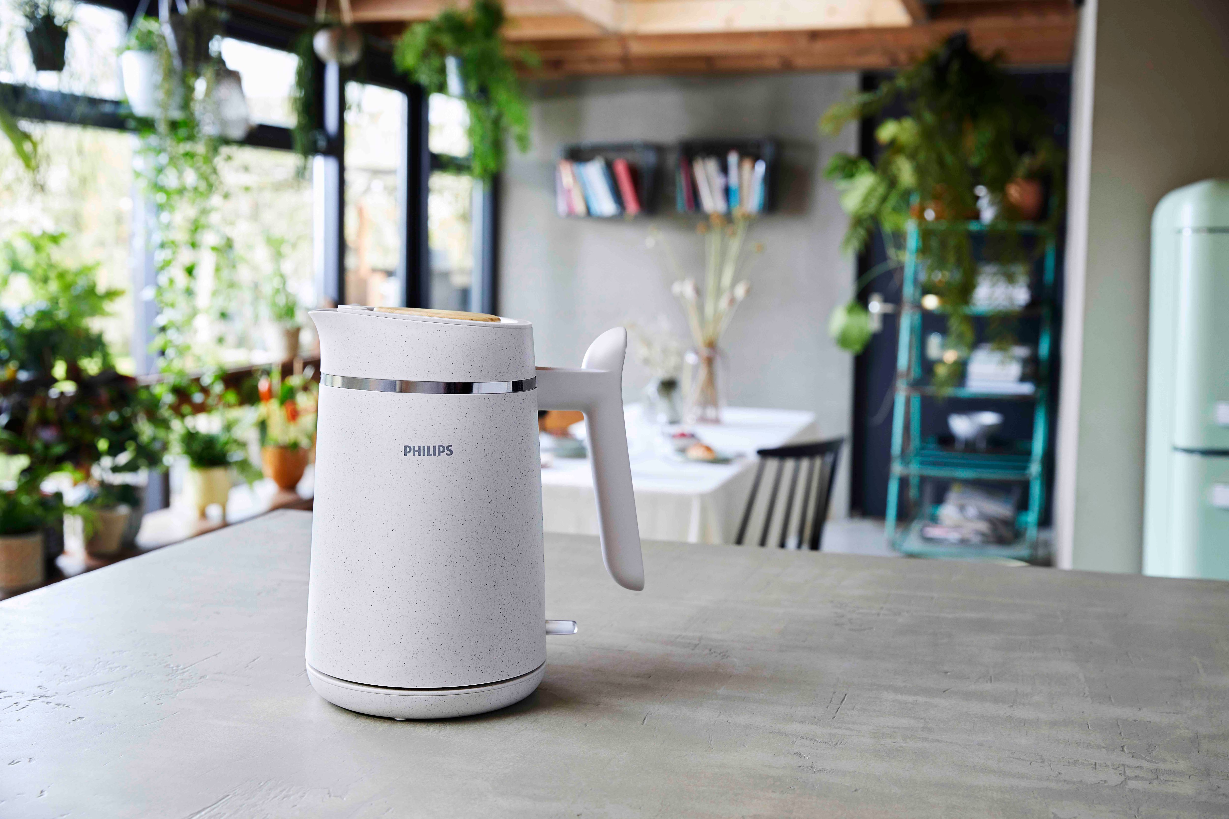 White Philips kettle on a kitchen counter, with plants and a table in the background.