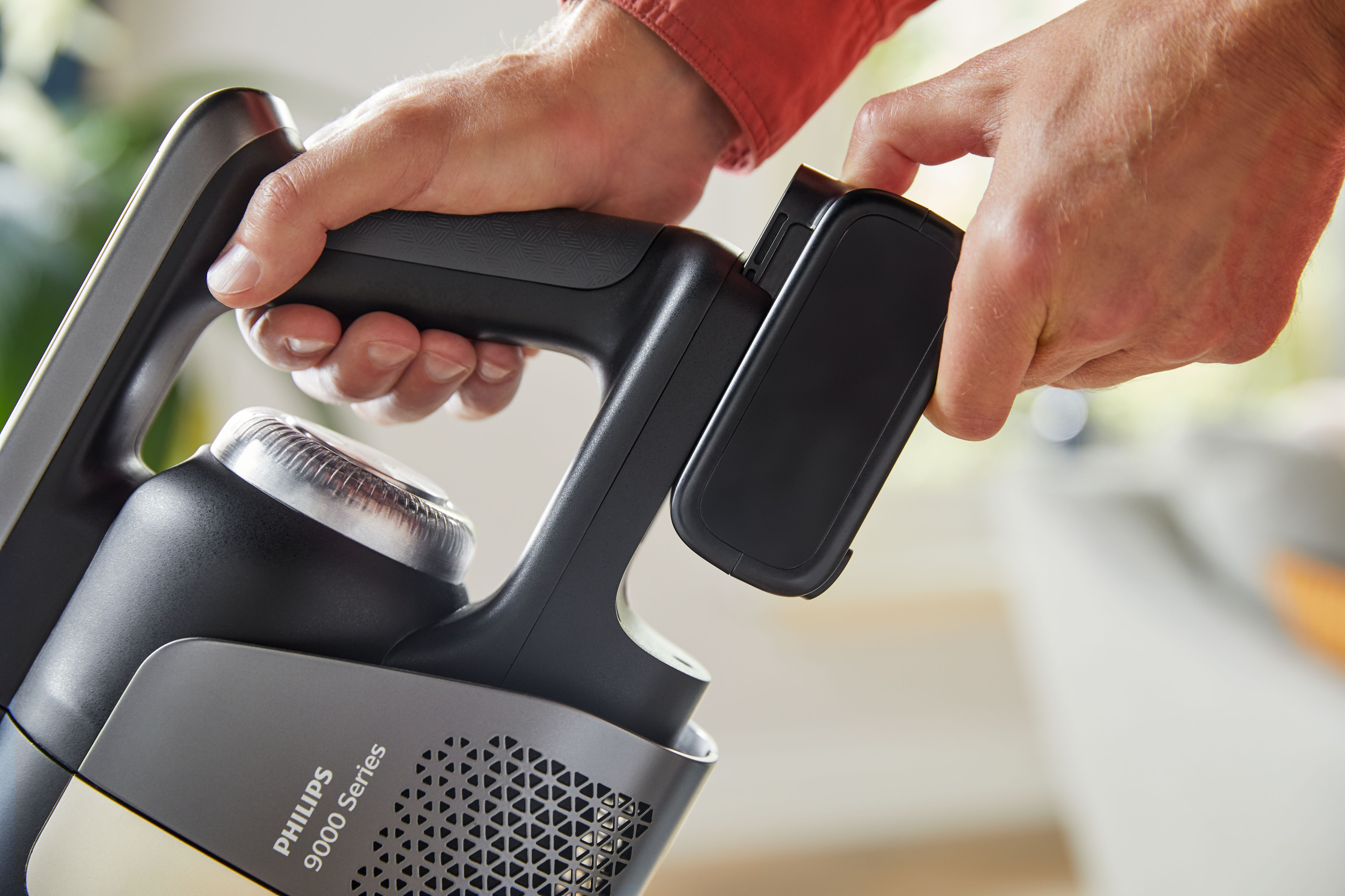 Handen bevestigen een batterij aan een Philips stofzuiger. De stofzuiger is grijs en zwart.