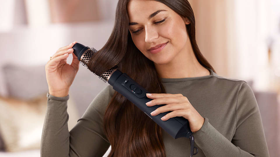 Woman using a black Philips hair styler on brown hair. Blurred background.