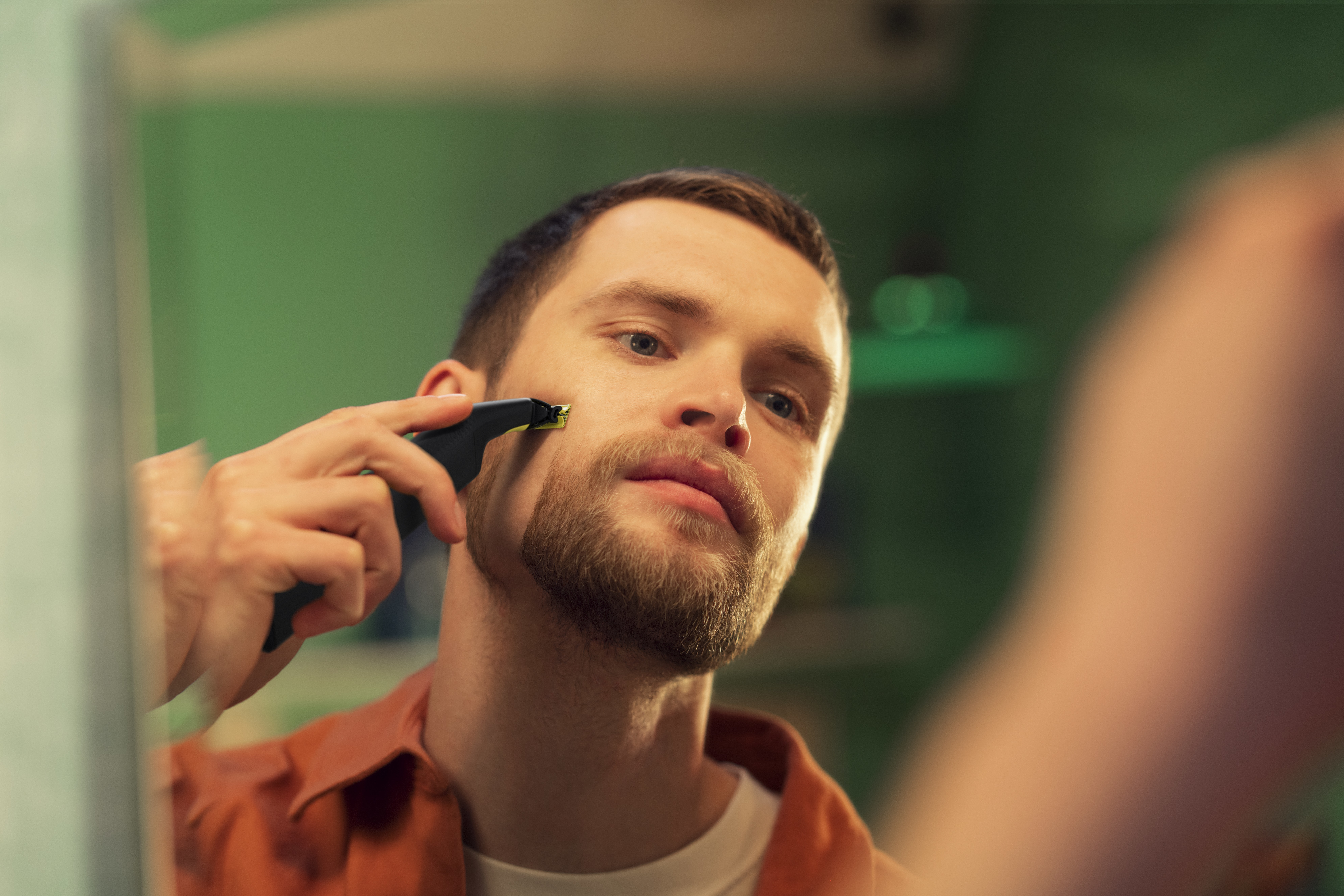Man scheert zijn baard in de spiegel met een elektrisch scheerapparaat.