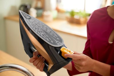 Person holding a black iron. Gold accents, yellow button, wood countertop.