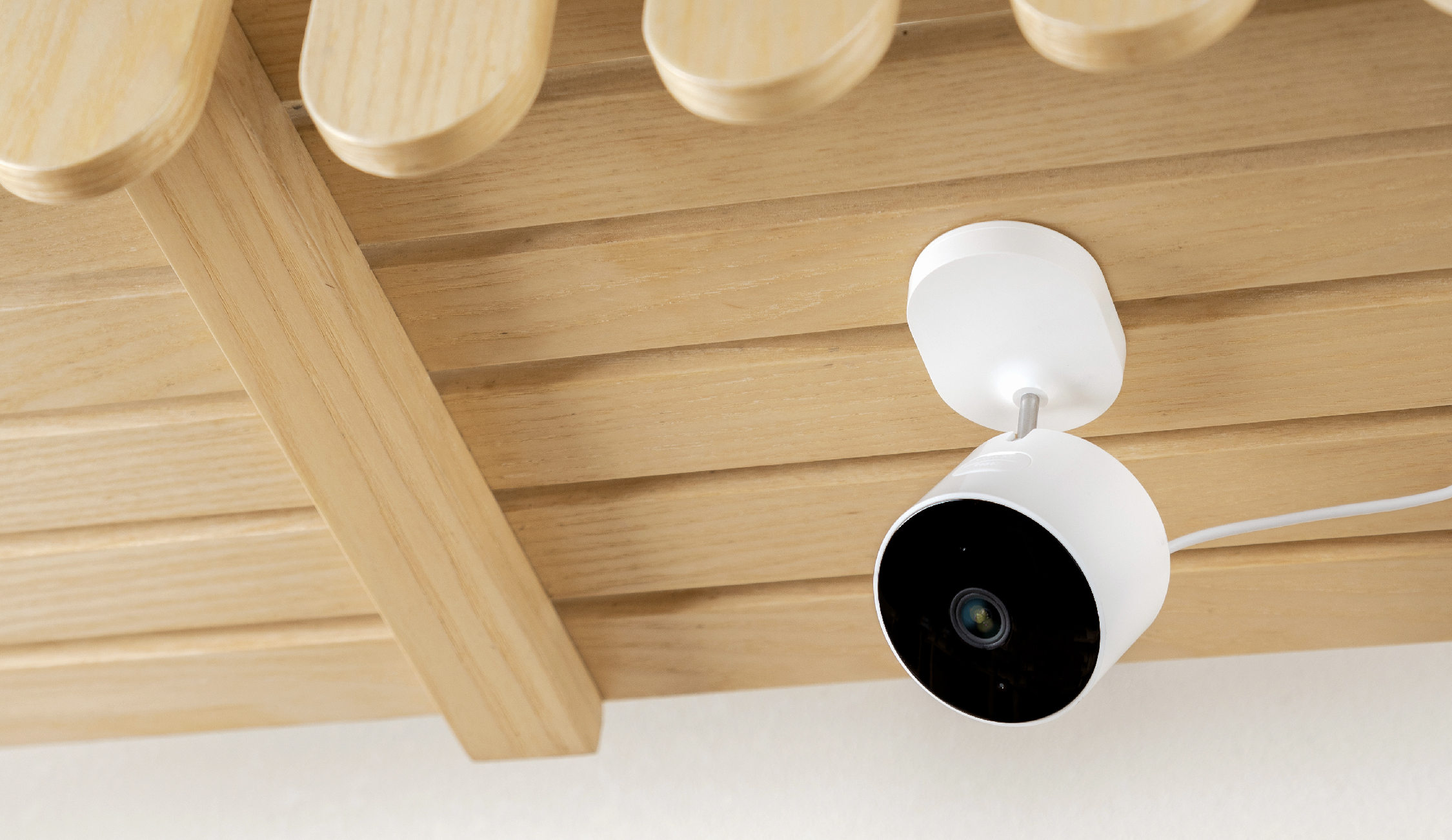 Una telecamera di sicurezza bianca è montata su pannelli di legno, rivolta verso il basso.
