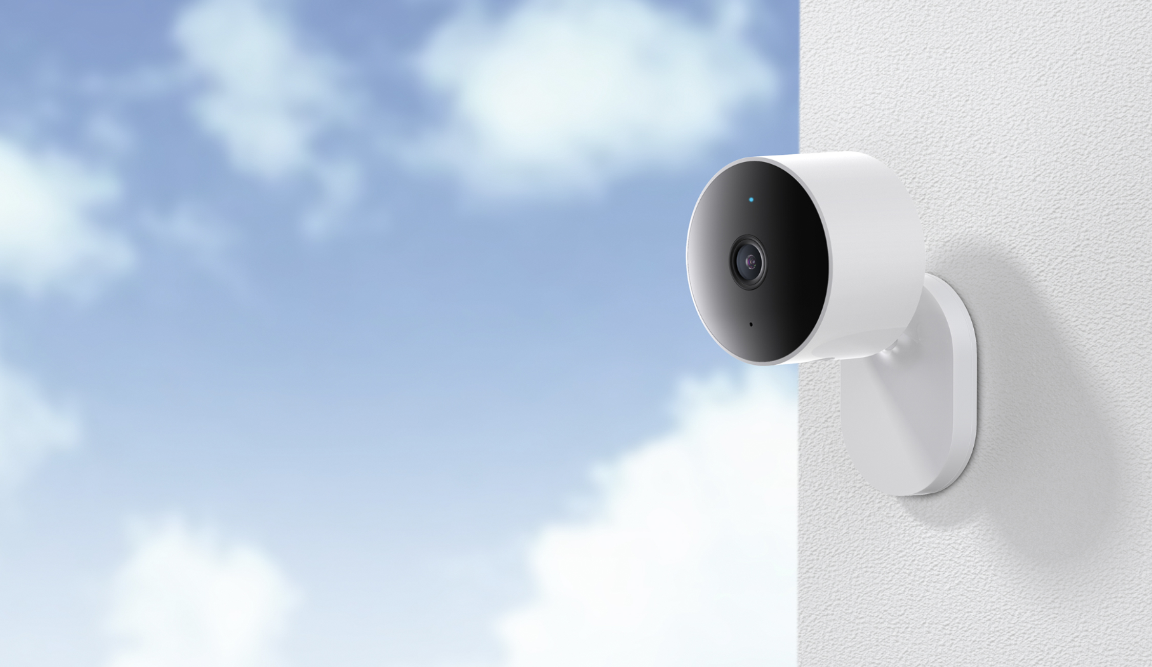 Telecamera di sicurezza bianca montata su muro bianco, cielo blu nuvoloso sullo sfondo.