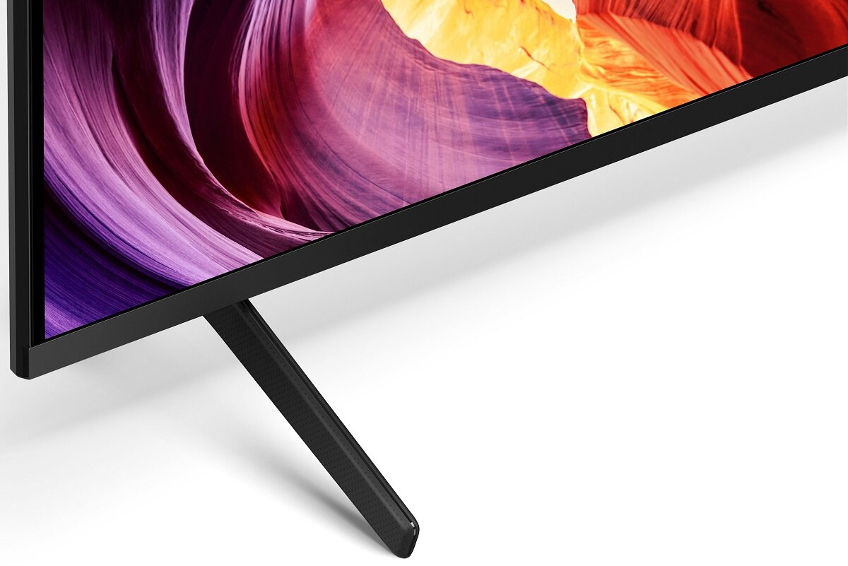 Zbliżenie rogu telewizora. Ekran wyświetla kolorowy obraz. Telewizor ma czarną ramę i podstawę.