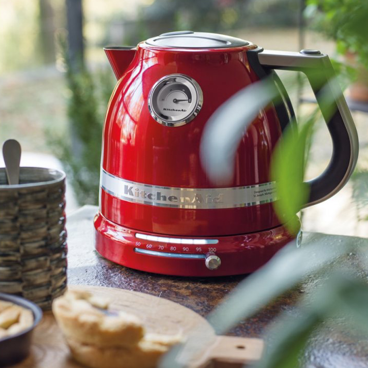 Bollitore elettrico KitchenAid rosso su un piano di lavoro. Ha un indicatore di temperatura e un manico nero.