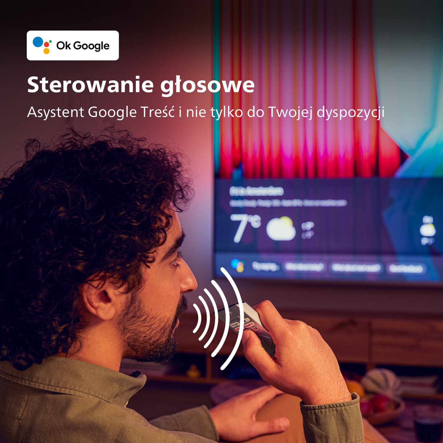 Mężczyzna używający pilota przed telewizorem. Tekst mówi: Sterowanie głosowe, Asystent Google.