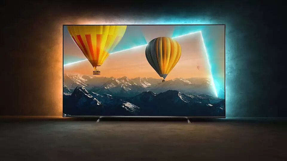 Telewizor z kolorowymi balonami na ekranie. Niebieskie i pomarańczowe akcenty świetlne. Ciemne tło.