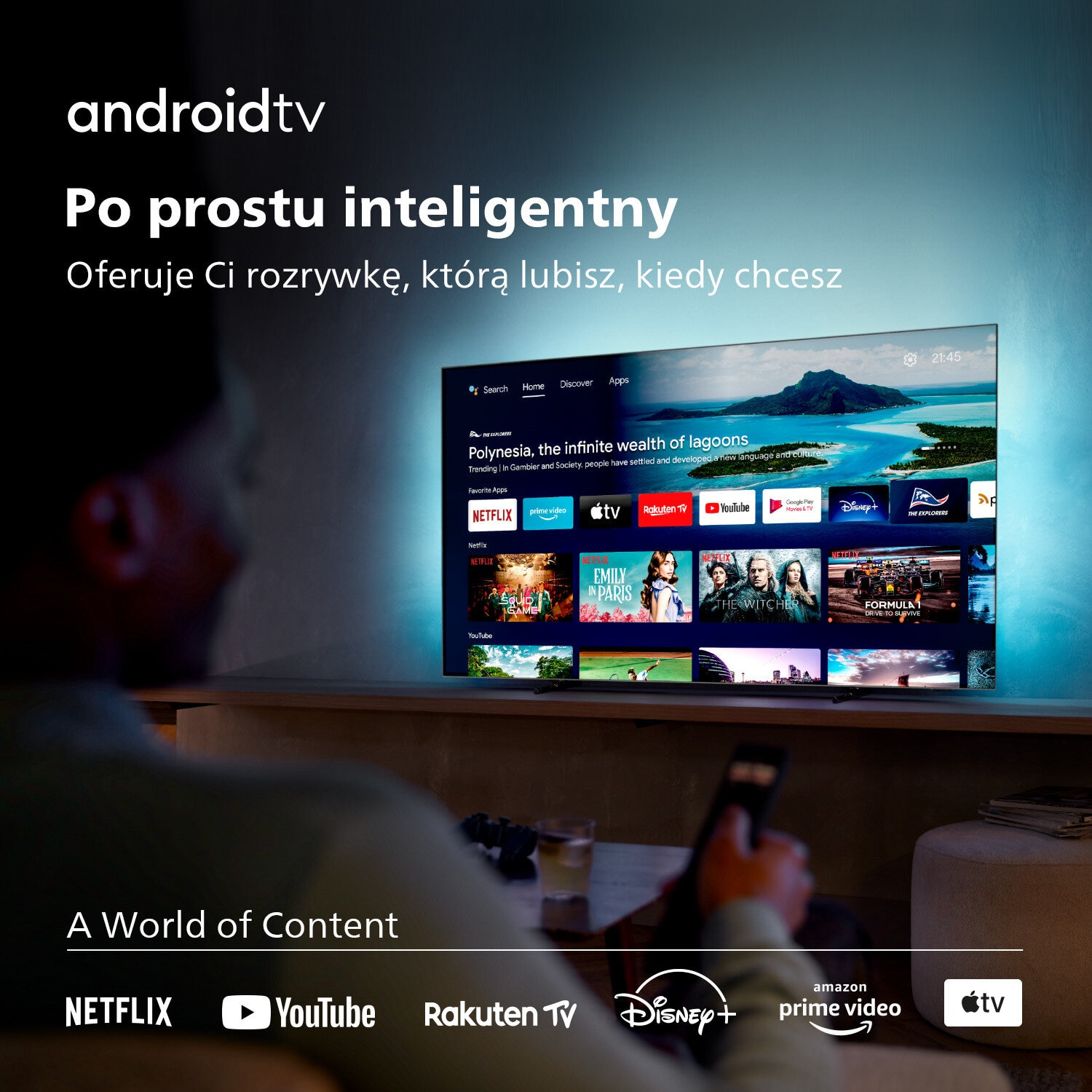 Interfejs Android TV na ekranie. Osoba trzyma pilota. Ikony treści na dole.
