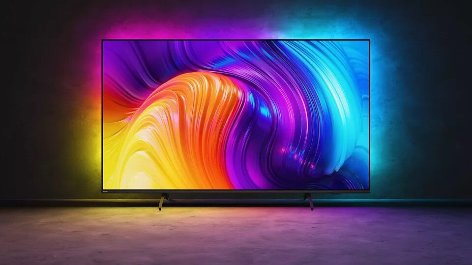 Duży telewizor wyświetlający kolorową sztukę abstrakcyjną, z oświetleniem otoczenia i ciemnym tłem.