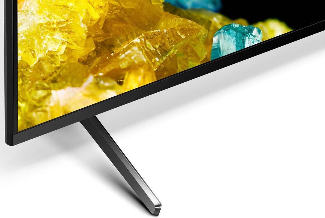 Zbliżenie rogu telewizora. Ekran pokazuje żółte i niebieskie abstrakcyjne kształty. Ma czarną ramkę i srebrną podstawę.