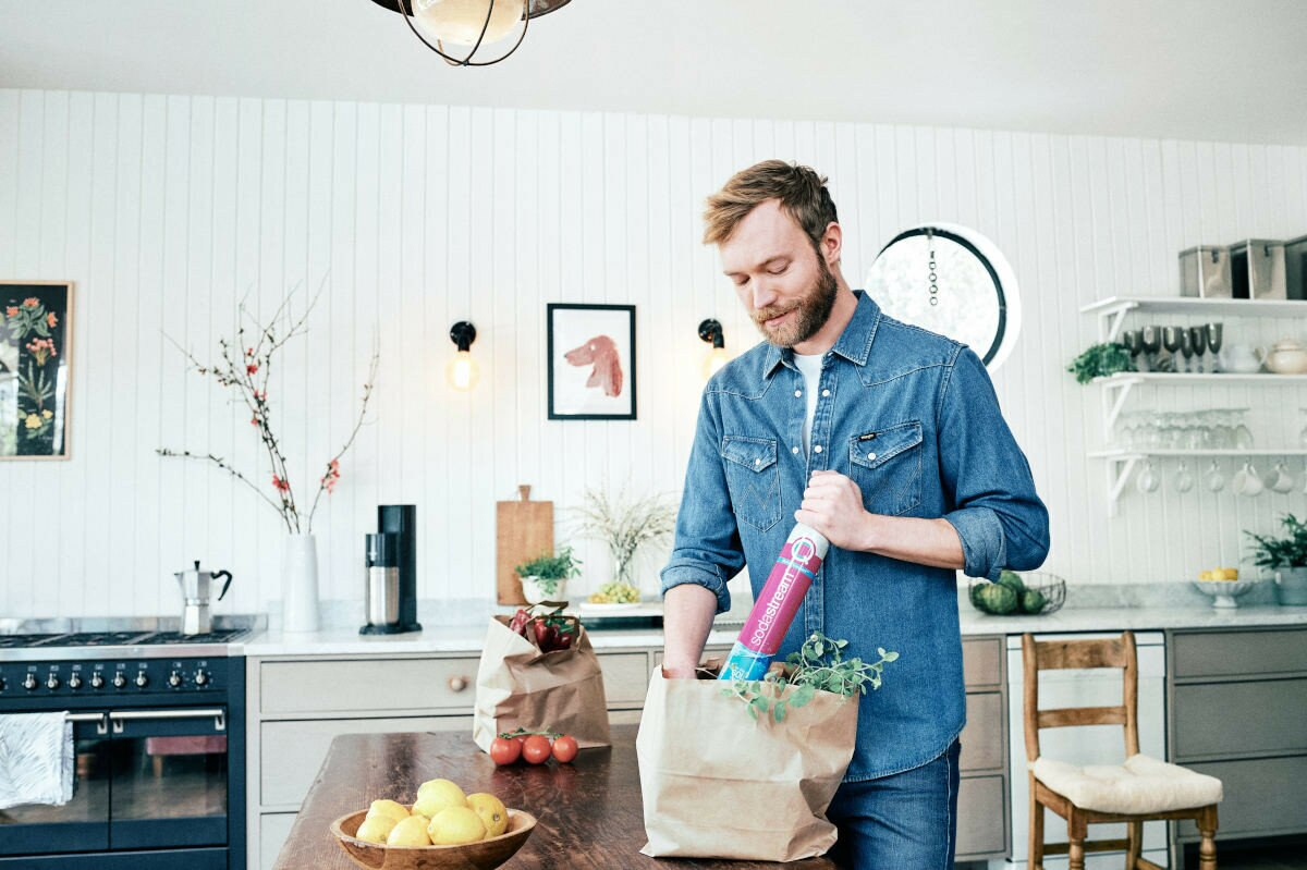 Mężczyzna w kuchni, wkładający artykuły spożywcze do papierowej torby. Wnętrze kuchni.