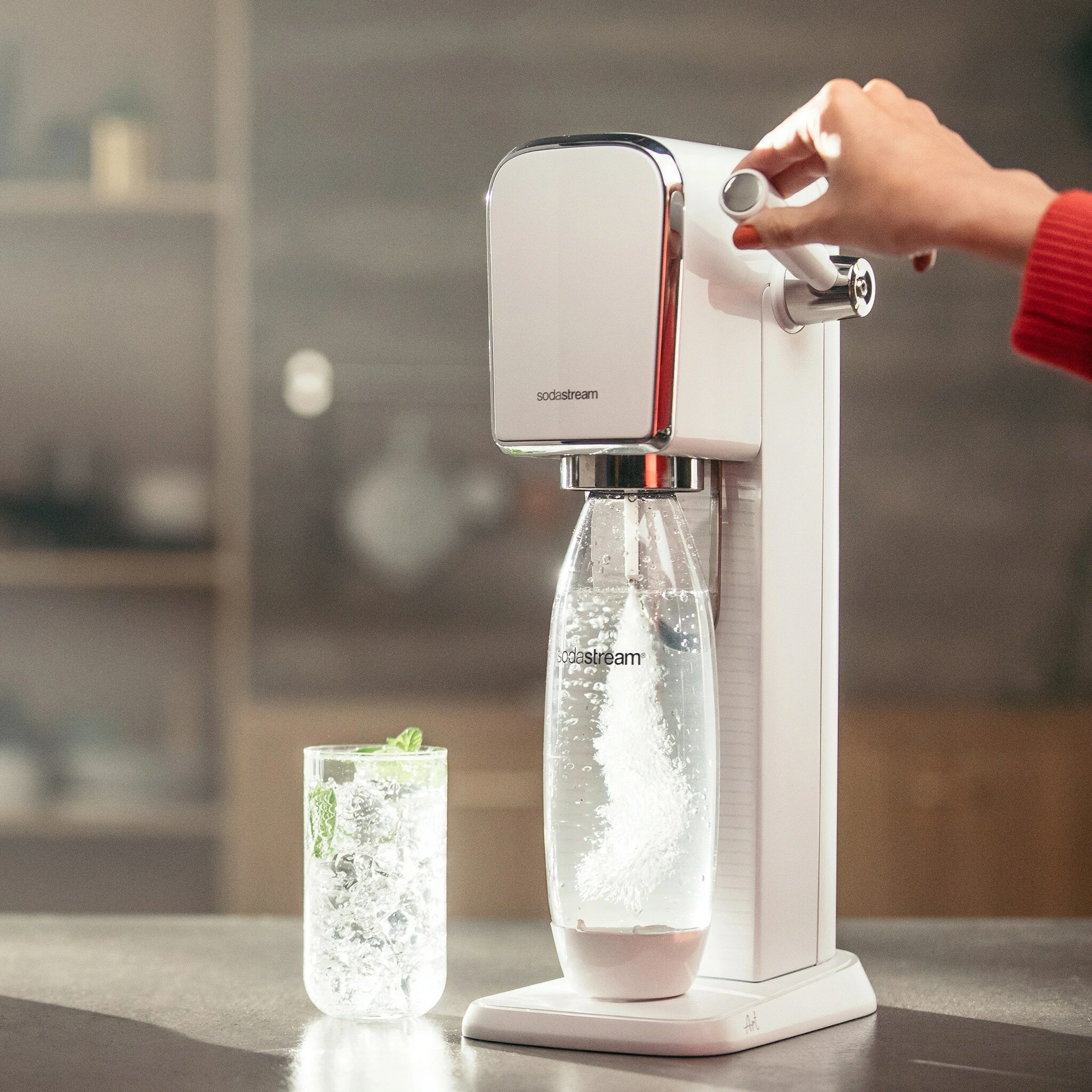 Maszyna SodaStream Duo z ręką obracającą dźwignię nasycania.