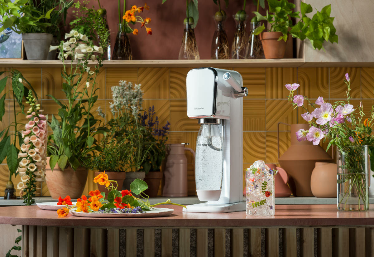 Biały ekspres do sody, kwiaty i rośliny na różowym blacie w kuchni.