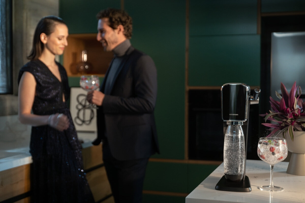 Para przygotowująca napoje z SodaStream. Szklanki z owocami i bąbelkami na blacie.